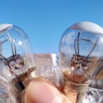 バルブの取り外し方法と、取り付け時の注意点  反論への理解:  主張:  理由:  具体例: そもそもですが、先ほどからバルブと呼んでいますが、電球のことです。 バルブと聞くと蛇口のようなものを想像すると思いますが、それは「valve」 電球は「bulb」で、これ自体にも電球という意味を持ちます。 (広義的には「球状のもの」ですね。) 家庭用の電球をバルブと呼ぶことは少ないですが、 車ではバルブという言葉をよく使います。 バルブの接続部を見ると、下の写真のような形状をしています。 時計回りで「LOCK」と書いていますね。 半時計周りに90°回すと、ソケットが外れます。 この状態ですね。 バルブも半時計周りに回すと外れます。 この時、軽く押しながら回しましょう。 ソケットの形状は以下のような感じです。 少し押さないとロックが外れない形状なのがわかりますね。 (押せるのか??と思うかもしれませんが、接続面の下にバネが入っており フカフカしているので、弱い力でも押せます。) 外したバルブと新品のバルブを比べてみましょう。 右側の古いバルブは、上側のフィラメントが切れているのがわかりますね。 フィラメントが2つある理由は、後程解説します。 そして、新しいバルブを取り付け、点灯試験をしましょう。 取り付ける際の注意点ですが、バルブを直接素手で触らないようにしましょう。 手の皮脂や油分が付くと悪影響が出ます。 ガラス部は高温となるため、熱が変質したり、その部分に熱が集中して バルブの寿命を縮める原因となります。 また金属部は、接触不良の原因となります。(個人的には、コチラはそれほど気にする必要な無いと思っていますが。) キレイな手袋をはめるなどして、作業に当たりましょう。 (手袋が汚くて、手袋の汚れが付くのもNGです。 私は、バルブが入った袋を持って作業しているのは内緒です・・・ 当然、落とすと割れるので、気を付けましょう。) あとは逆の手順で取り付ければ作業完了です。 かなり簡単でサクッと作業できます